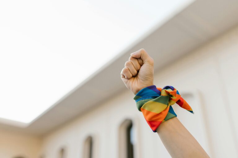 Close-up of a raised fist wearing a rainbow cloth, symbolizing LGBTQ+ pride and unity.